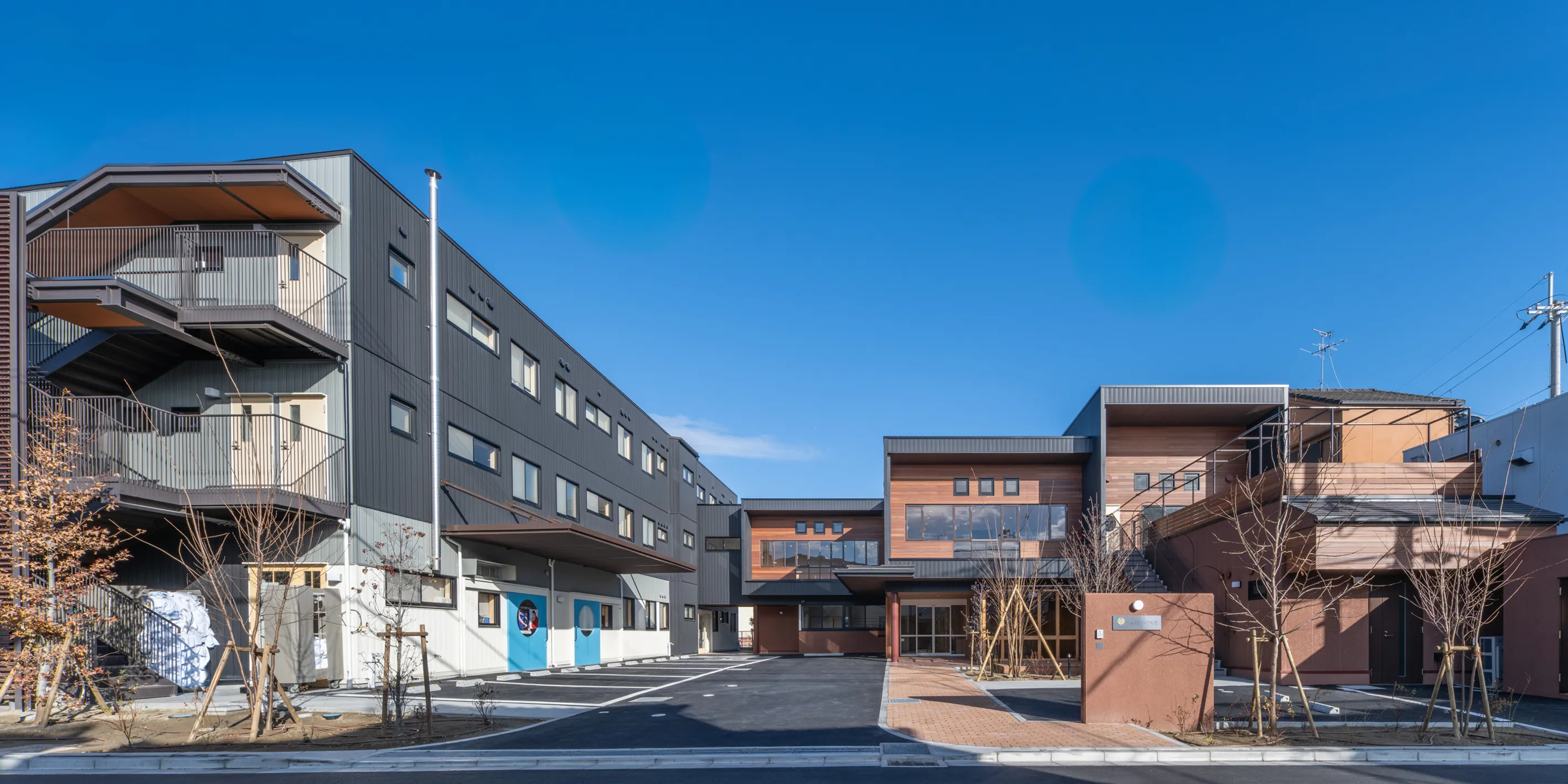 ジョブサイトひむろの外観。青空の下、左に3階建てのグレー色の建物、右に2階建ての温かみのあるオレンジ色の建物が建っている。